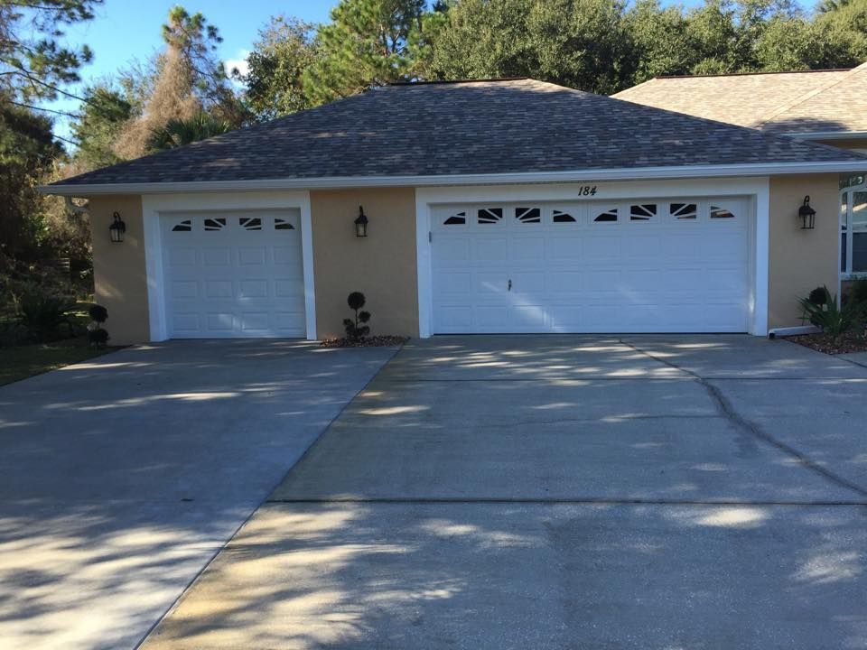 Two-car garage with two white doors, tan walls, and a gray roof, in front of a concrete driveway.
