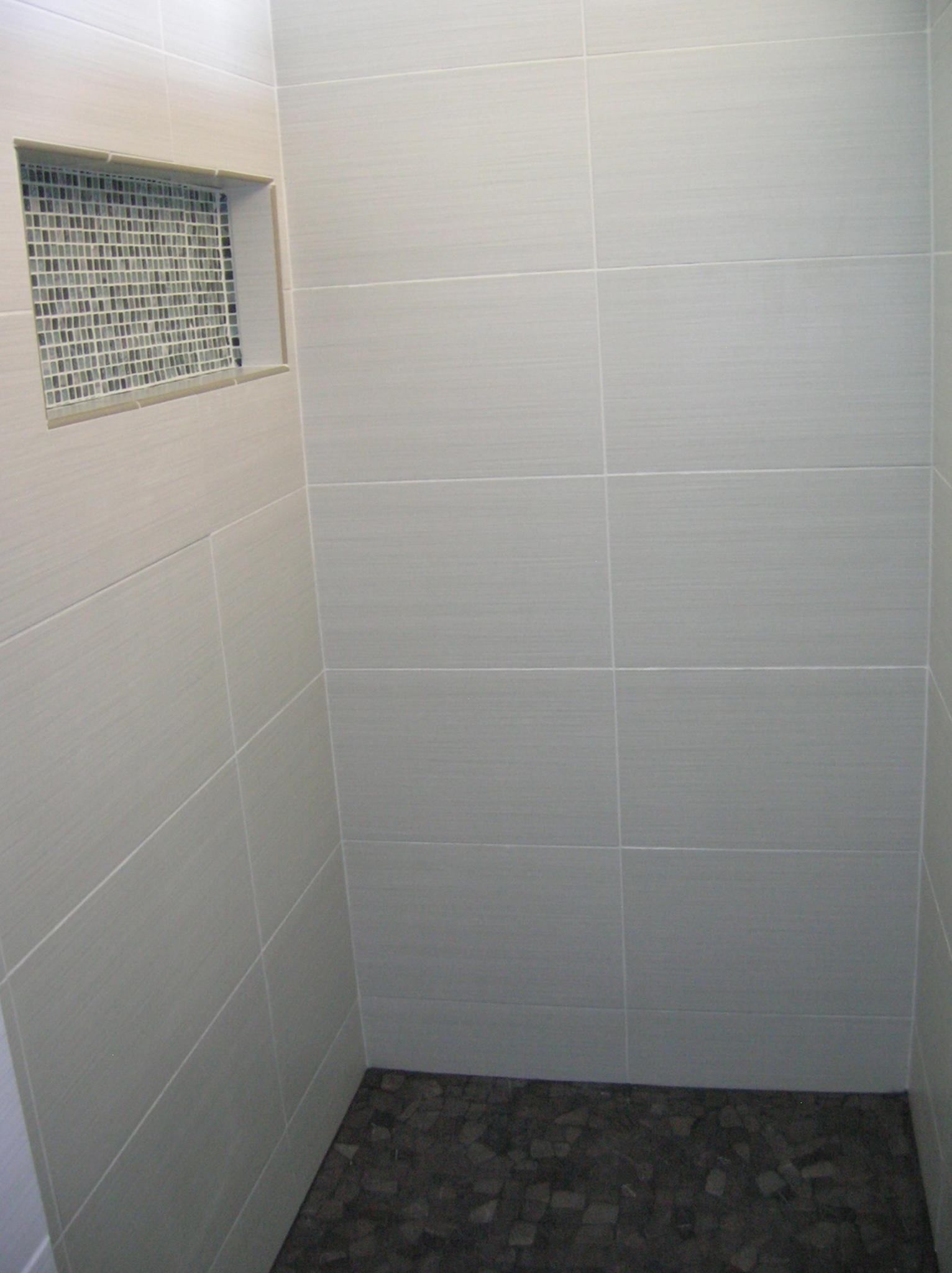 Tiled shower interior with pebble floor and decorative tile window.
