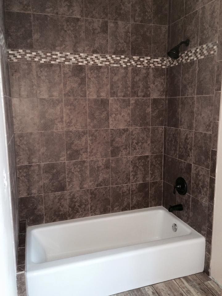 Bathroom shower with dark brown tiled walls, a white tub, and a decorative tile band.