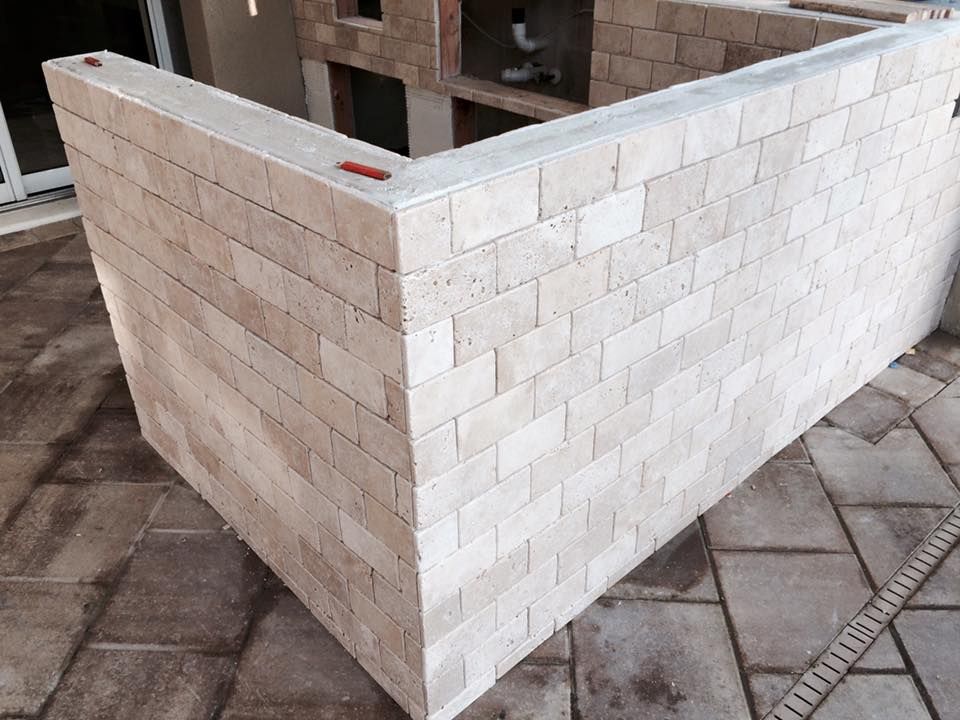Brick outdoor bar, beige bricks with gray concrete top, set on a patio with a drainage grate.