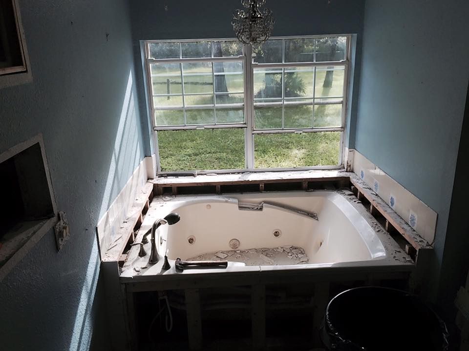 Bathroom renovation, bathtub beneath a window. Blue walls, partially demoed, awaiting new tile or surround.