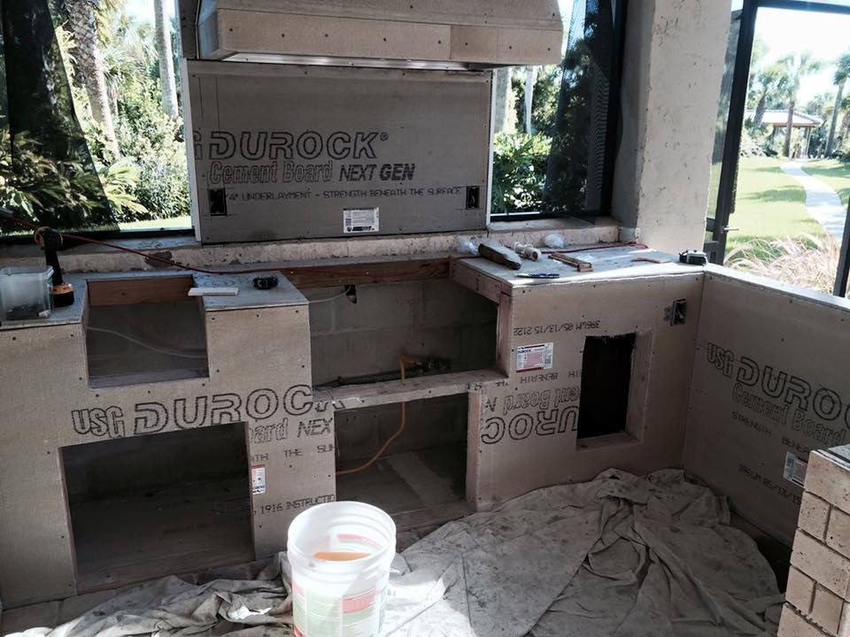 Outdoor kitchen under construction, covered in gray Durock, with openings for appliances, and a window.