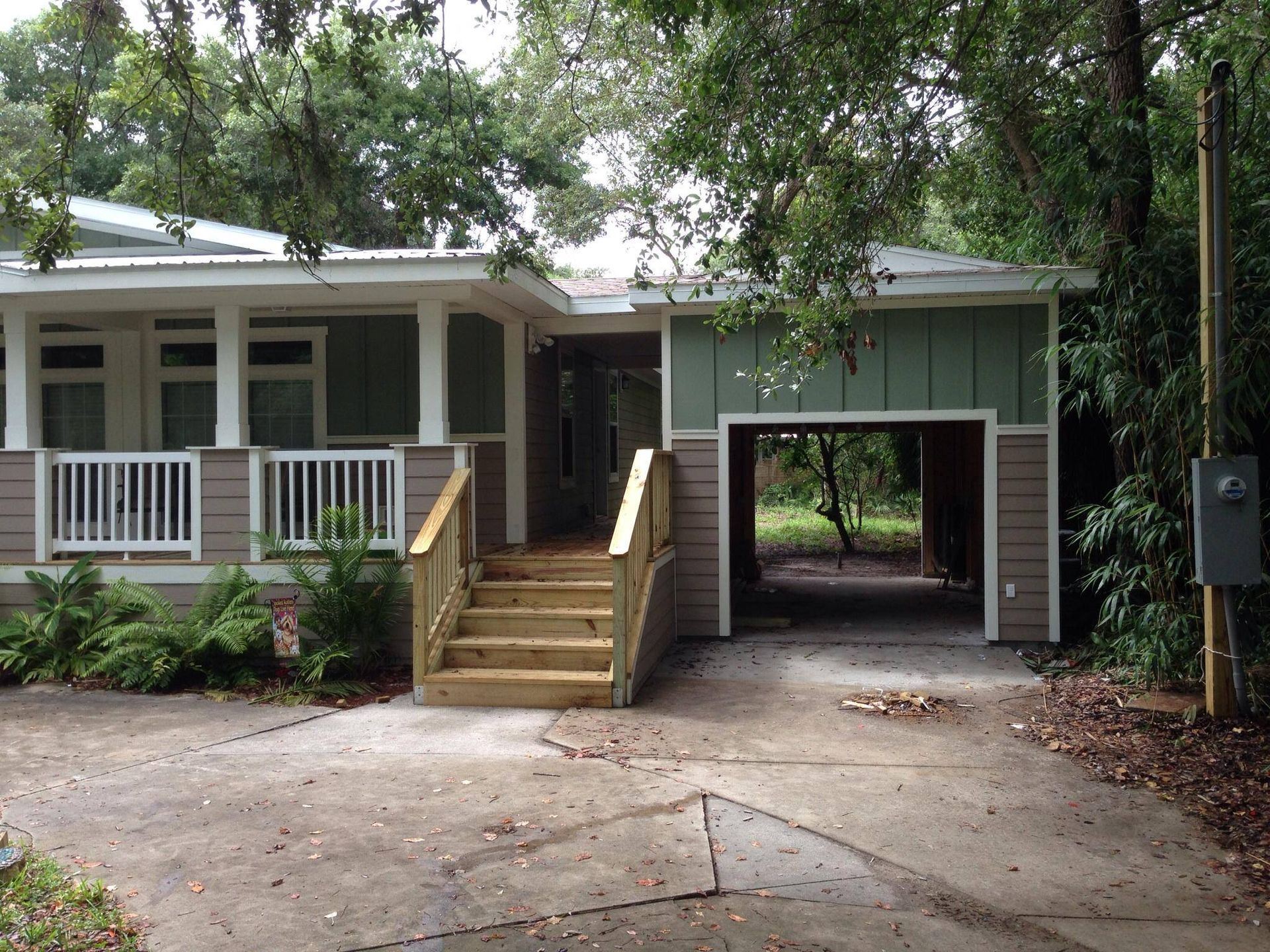House with porch and carport, light green siding, wooden stairs, concrete driveway.