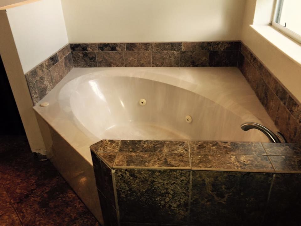 Corner jacuzzi tub surrounded by brown tiled trim and a window.