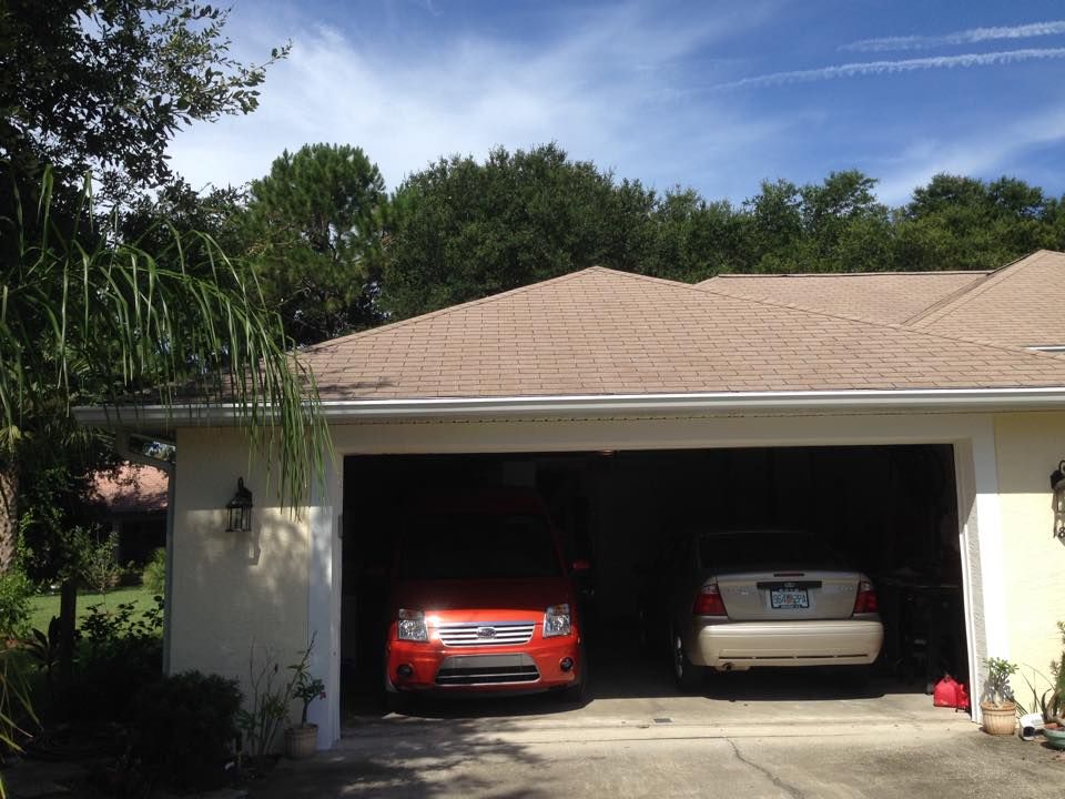 Two cars parked in a garage under a tan roof. Bright orange car, beige car, blue sky.