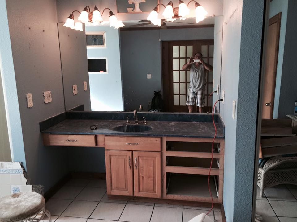 Bathroom vanity under renovation with a person in the mirror. Cabinets, countertop, and mirror are visible.