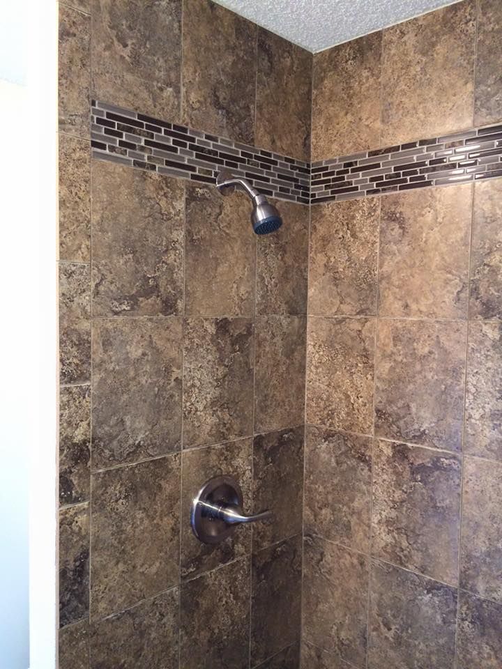 Brown tiled shower with mosaic tile border, chrome shower head and handle.