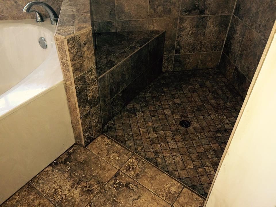 Bathroom with brown tiled shower and built-in bench next to a white bathtub.