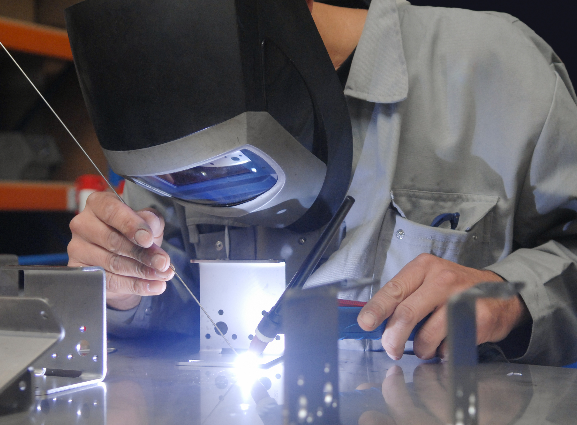 A man wearing a welding mask is welding a piece of metal
