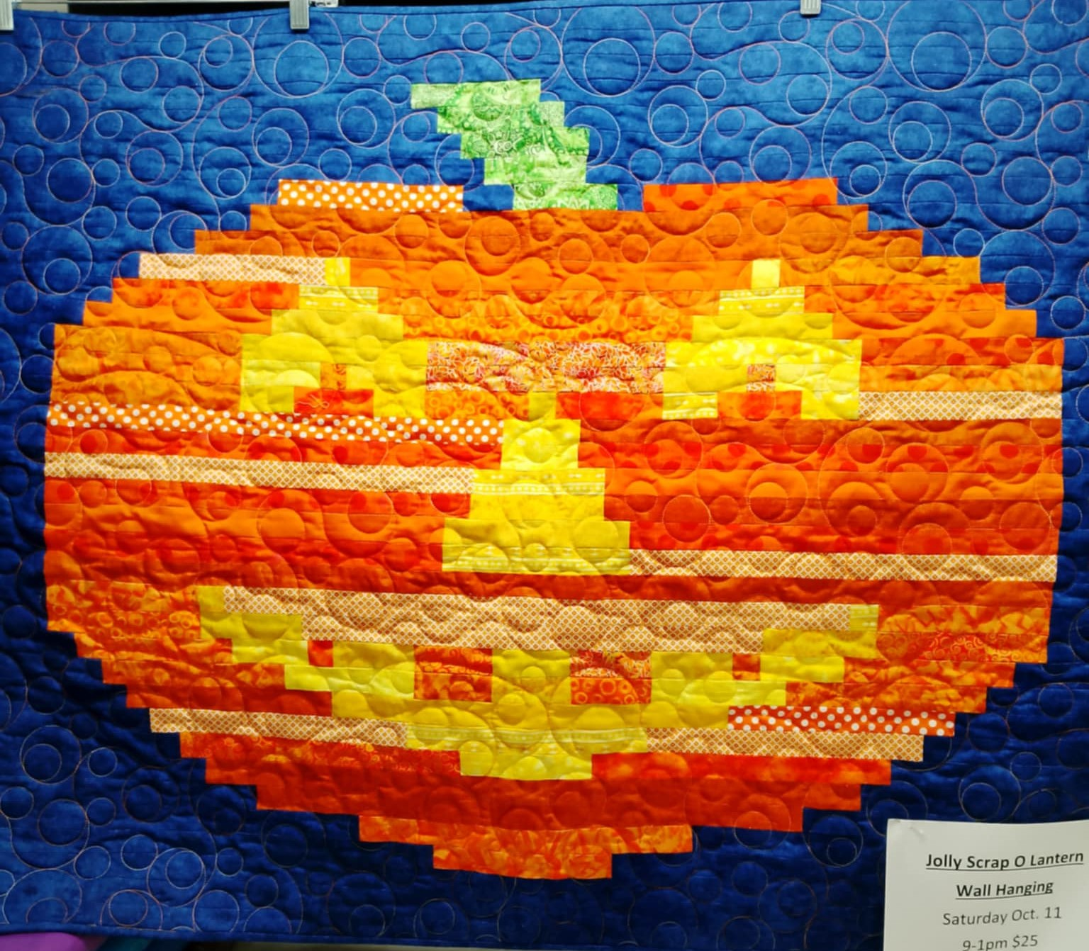 Quilted orange pumpkin with a carved face on blue background.