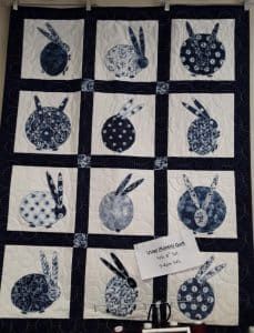 A quilt with rabbits on it is hanging on a wall.