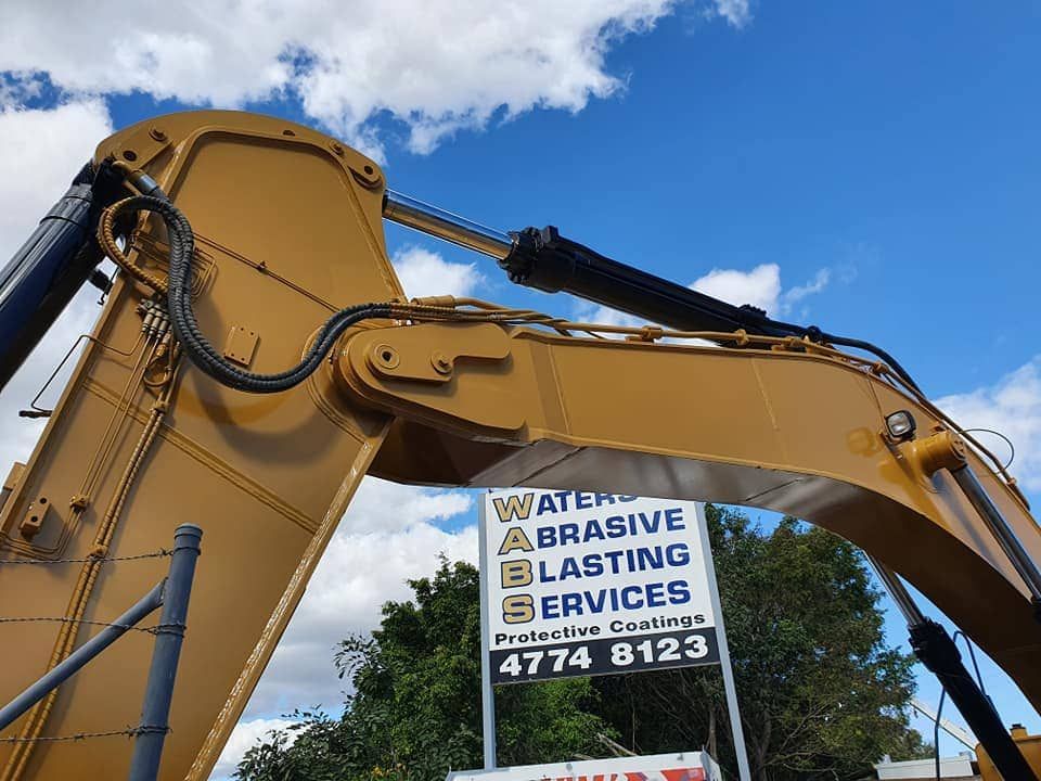 A Large Yellow Excavator With a Sign That Says Water Abrasive Blasting Services — Waters Abrasive Blasting Services In Cairns, QLD