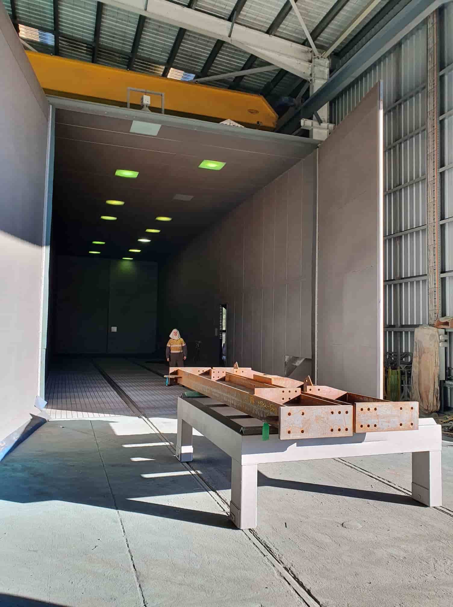 A Large Warehouse With a Crane in the Background and a Table in the Foreground — Waters Abrasive Blasting Services In Shaw, QLD