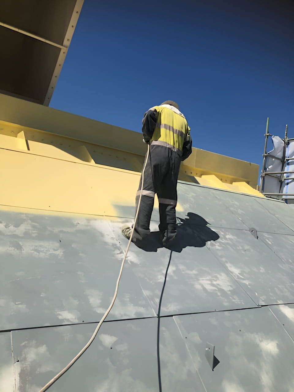 A Man is Standing on Top of a Roof Painting It Yellow — Waters Abrasive Blasting Services In Townsville, QLD