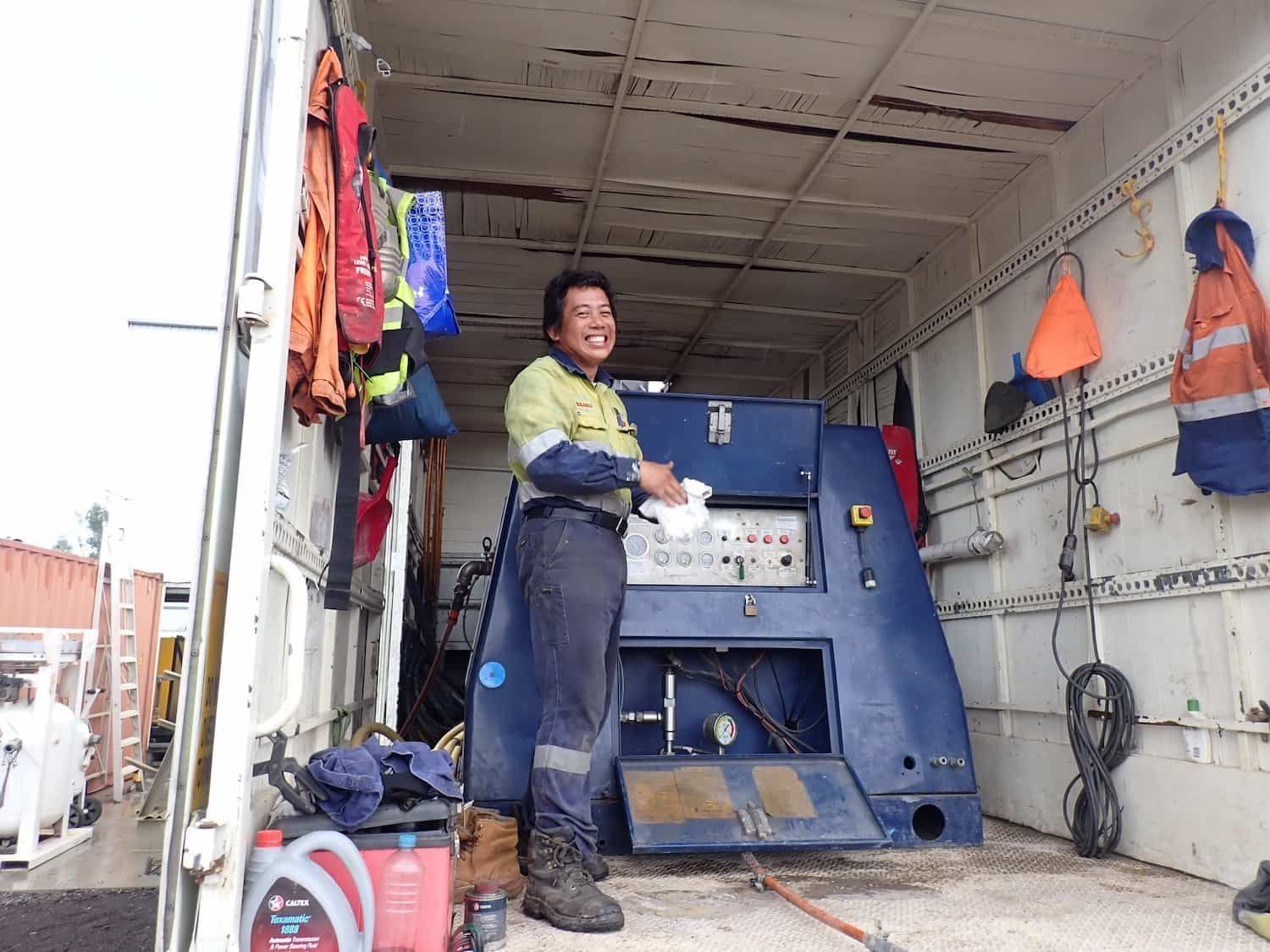 A Man is Standing in the Back of a Truck Next to a Machine — Waters Abrasive Blasting Services In Shaw, QLD