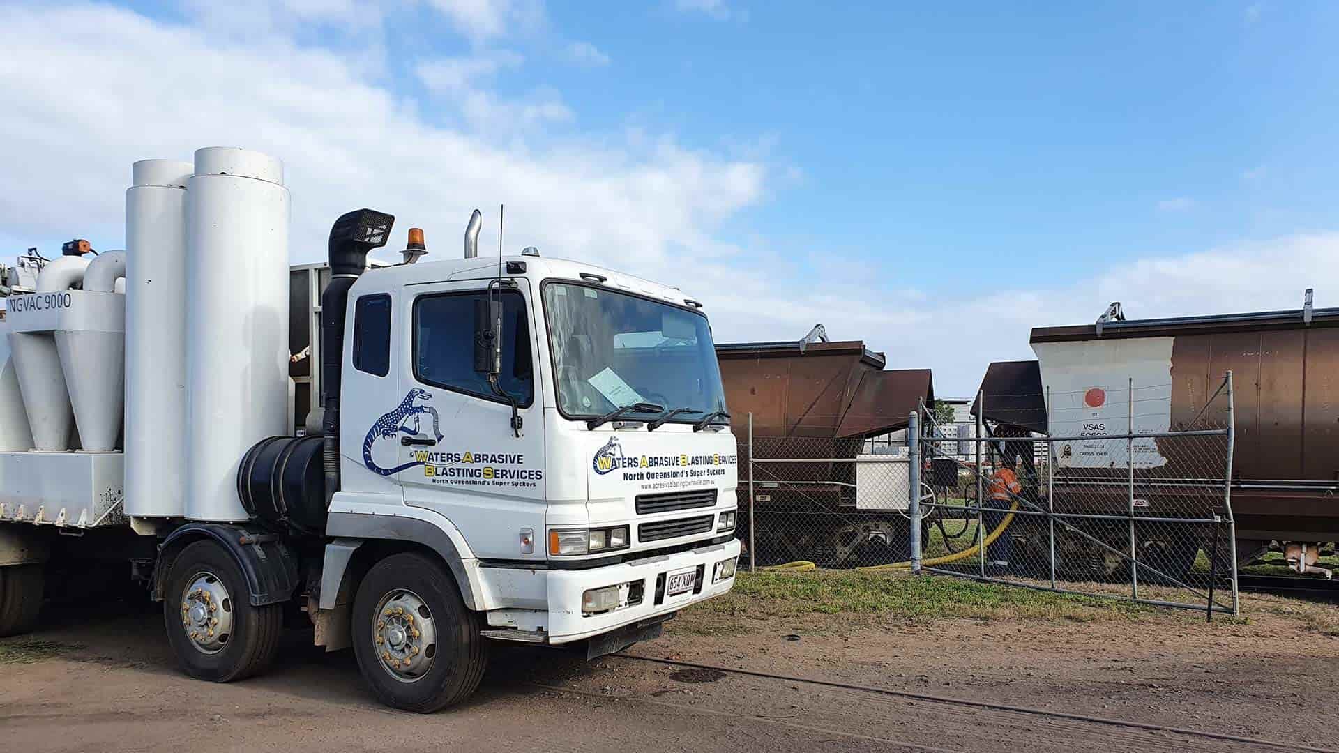 A White Truck is Parked in a Dirt Lot Next to a Train — Waters Abrasive Blasting Services In Shaw, QLD