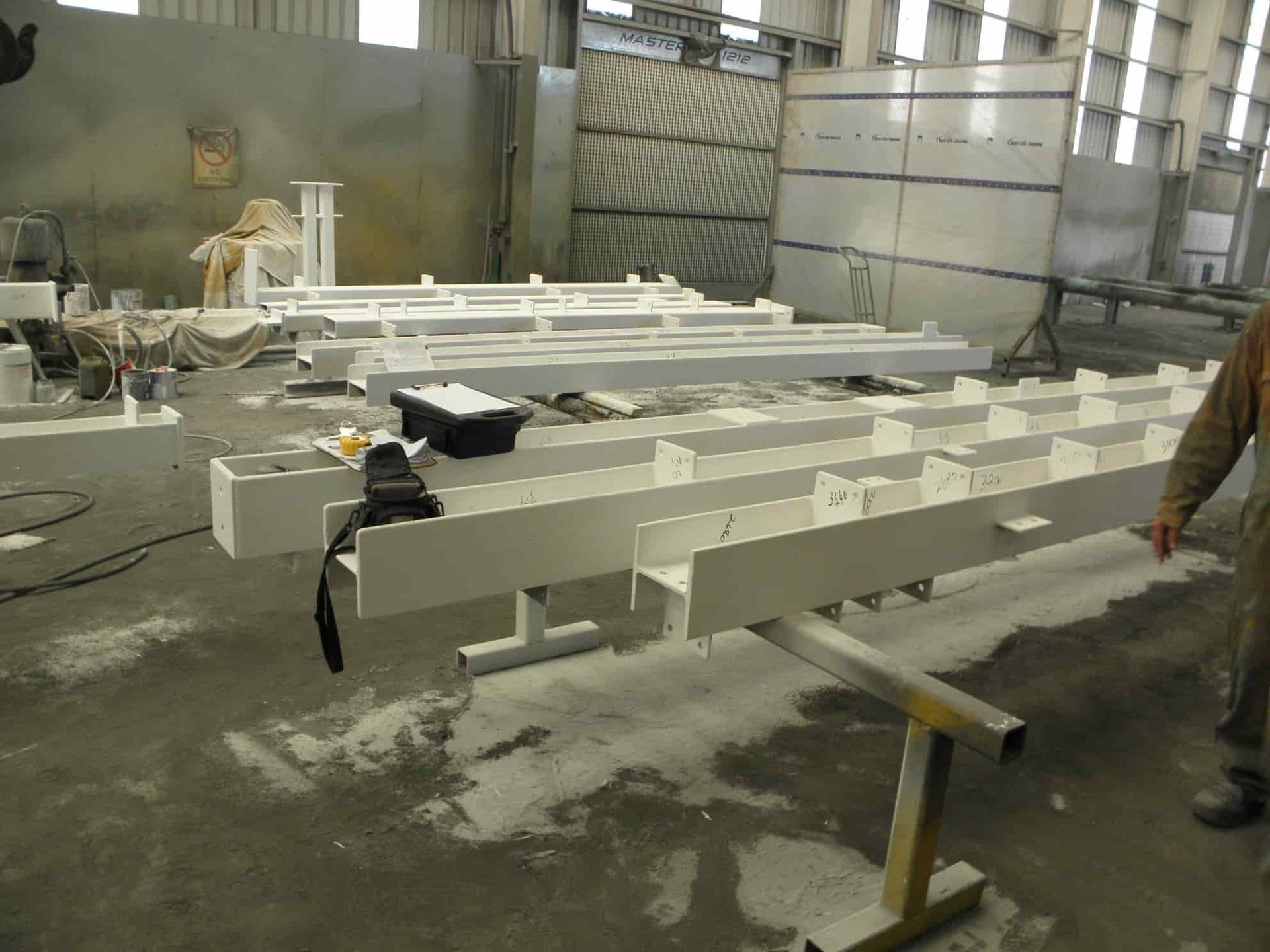 A Man is Standing in a Room With a Lot of White Pieces of Metal — Waters Abrasive Blasting Services In Shaw, QLD