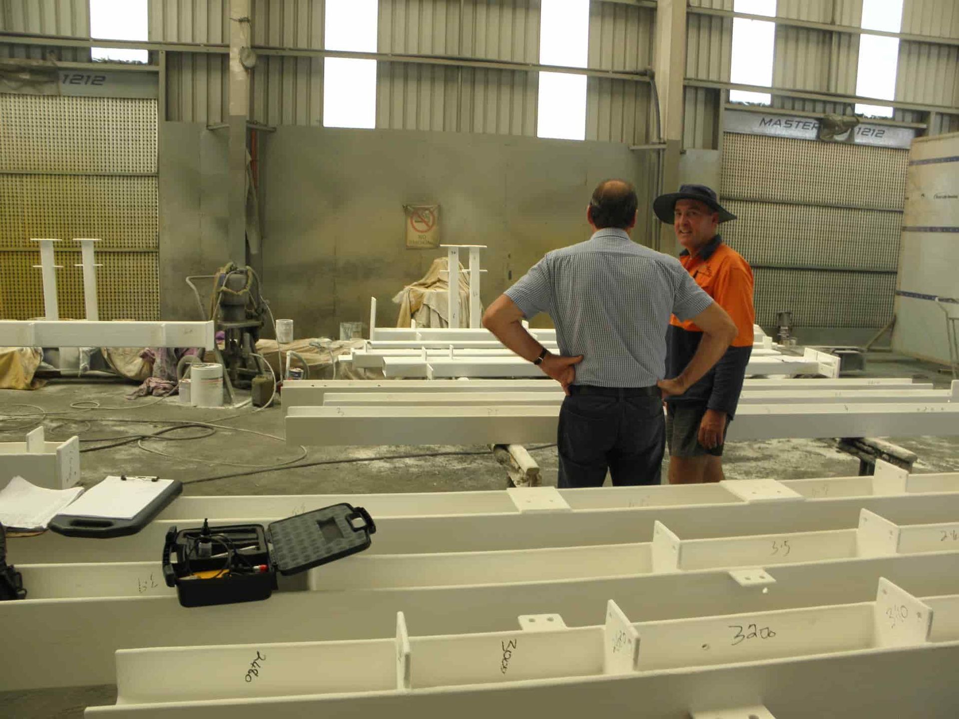 Two Men Are Standing Next to Each Other in a Warehouse — Waters Abrasive Blasting Services In Shaw, QLD