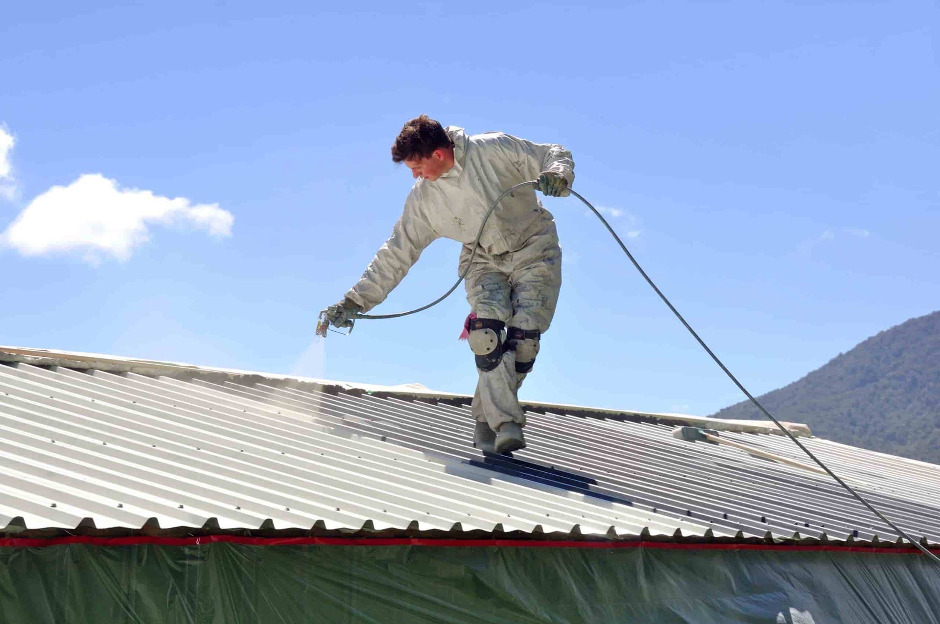 A Man is Spraying Paint on the Roof of a Building — Waters Abrasive Blasting Services In Shaw, QLD