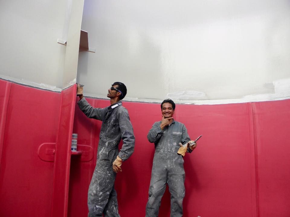 Two Men Are Standing Next to Each Other Painting a Red Wall — Waters Abrasive Blasting Services In Bundaberg, QLD