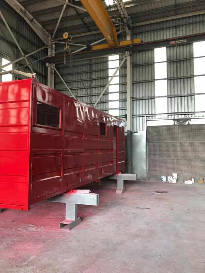 A Large Red Container is Sitting in a Warehouse Under a Crane — Waters Abrasive Blasting Services In Shaw, QLD