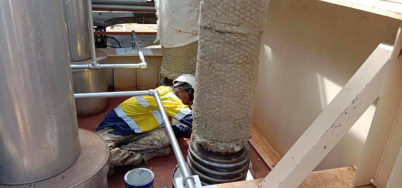A Man is Kneeling Down Next to a Pipe in a Room — Waters Abrasive Blasting Services In Darwin, NT