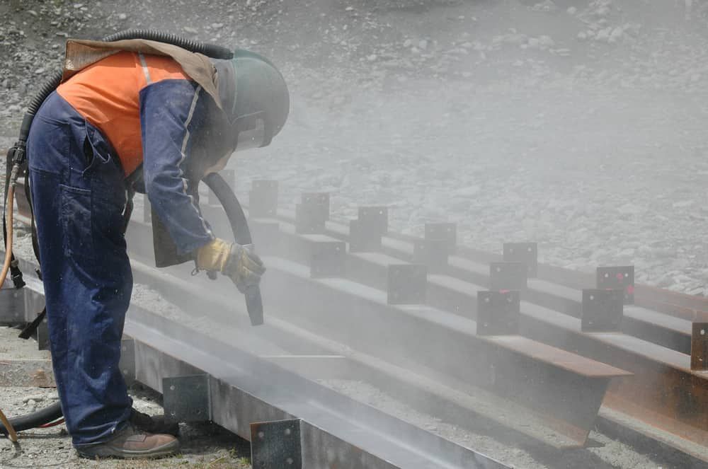 A Man is Sandblasting a Piece of Metal — Waters Abrasive Blasting Services In Shaw, QLD