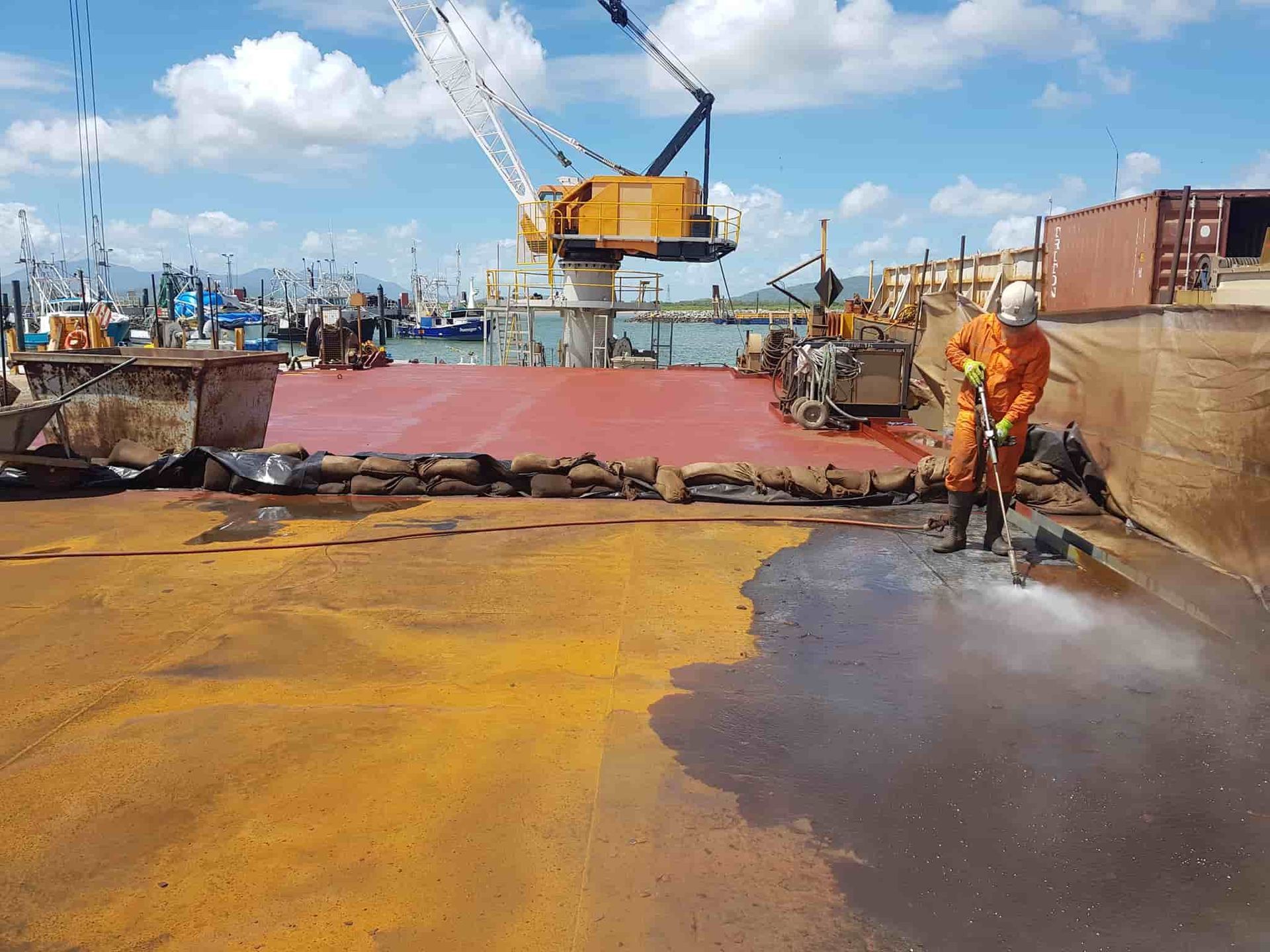 A Man is Spraying Water on a Boat in a Harbor — Waters Abrasive Blasting Services In Mackay, QLD