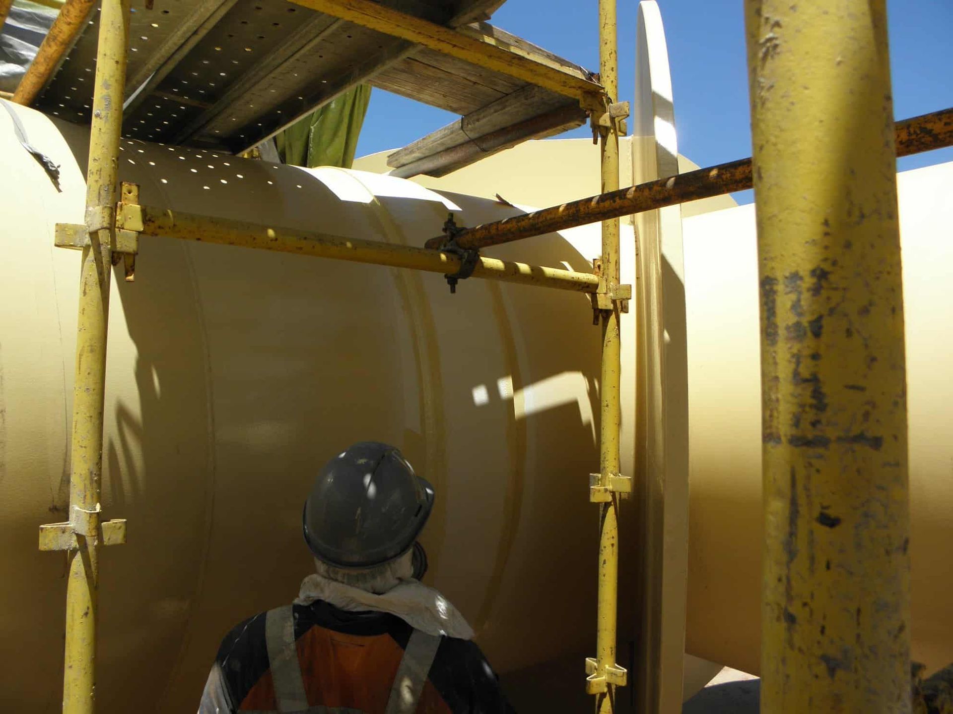 A Man Wearing a Hard Hat is Standing Under a Scaffolding — Waters Abrasive Blasting Services In Shaw, QLD