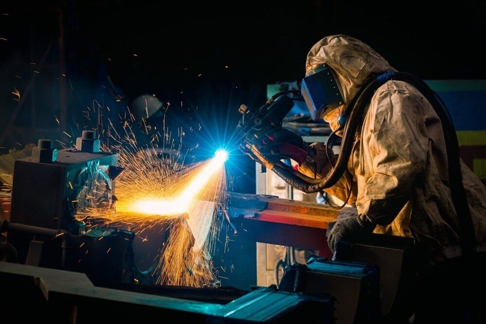 A Man is Welding a Piece of Metal in a Factory — Waters Abrasive Blasting Services In Shaw, QLD