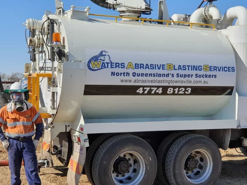 A Man Wearing a Mask is Standing Next to a Waters Abrasive Blasting Services Truck — Waters Abrasive Blasting Services In Shaw, QLD
