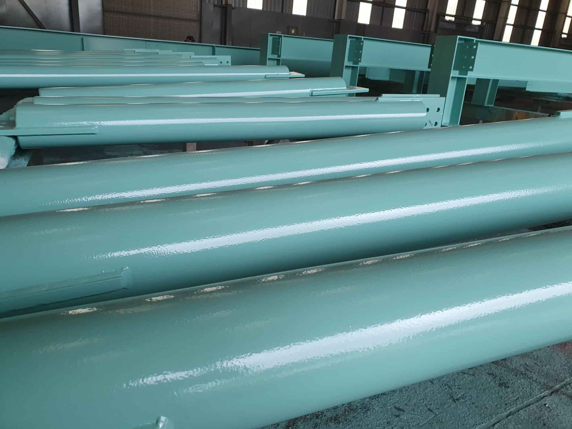 A Bunch of Green Pipes Are Stacked on Top of Each Other in a Building — Waters Abrasive Blasting Services In Shaw, QLD
