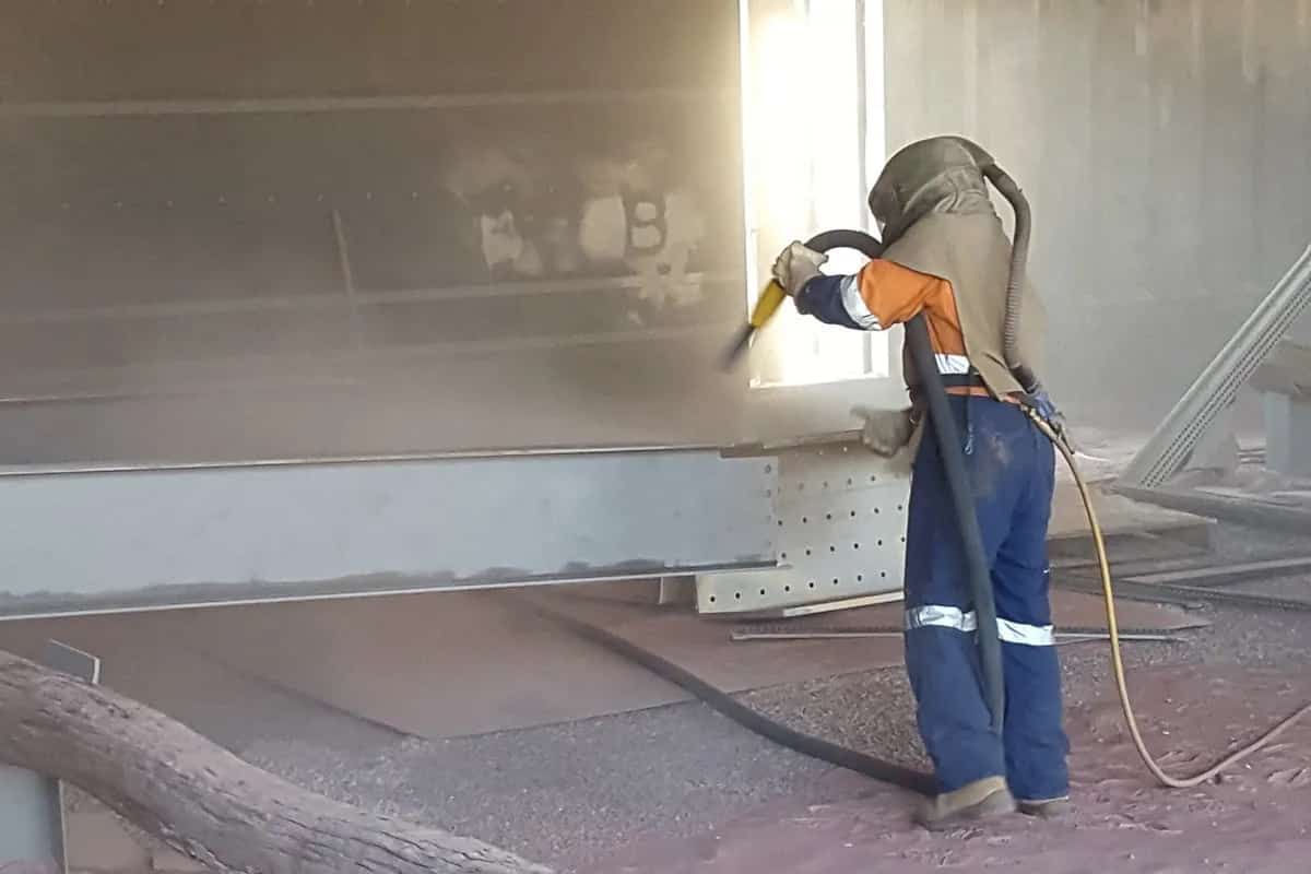 A Man is Wearing a Helmet and Using a Machine to Spray Paint a Wall — Waters Abrasive Blasting Services In Shaw, QLD