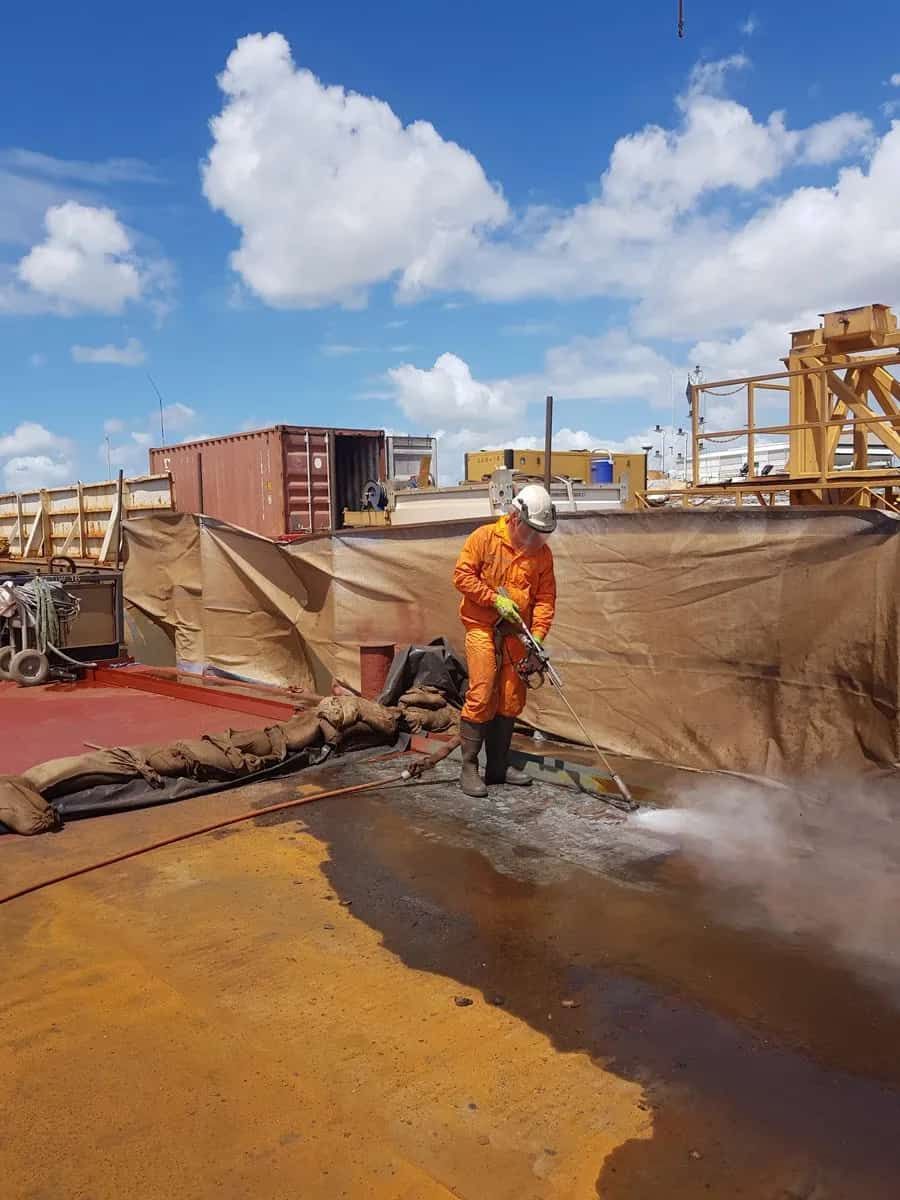 A Man in an Orange Jumpsuit is Standing in a Puddle of Water — Waters Abrasive Blasting Services In Shaw, QLD