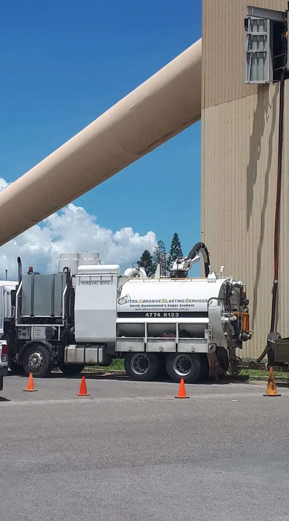 A Vacuum Truck is Parked in Front of a Large Building — Waters Abrasive Blasting Services In Shaw, QLD