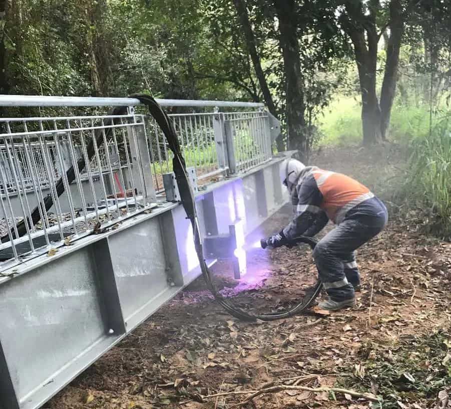 A Man is Welding a Metal Structure in the Woods — Waters Abrasive Blasting Services In Shaw, QLD