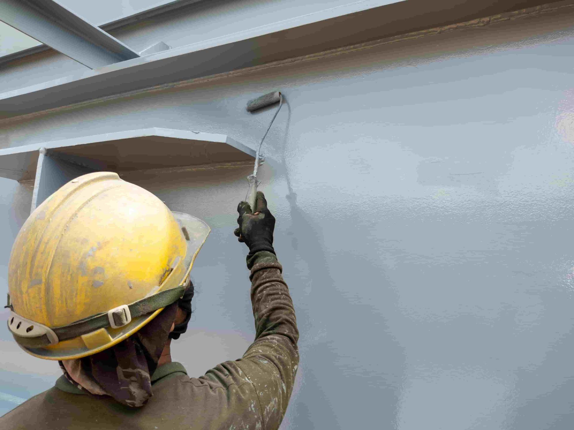 A Man Wearing a Hard Hat is Painting a Wall With a Roller — Waters Abrasive Blasting Services In Shaw, QLD
