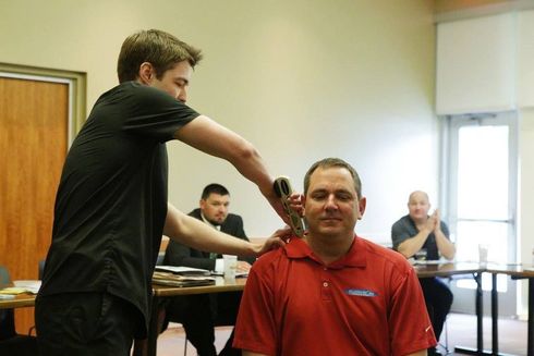 A man in a red shirt is getting his hair cut by a man in a black shirt