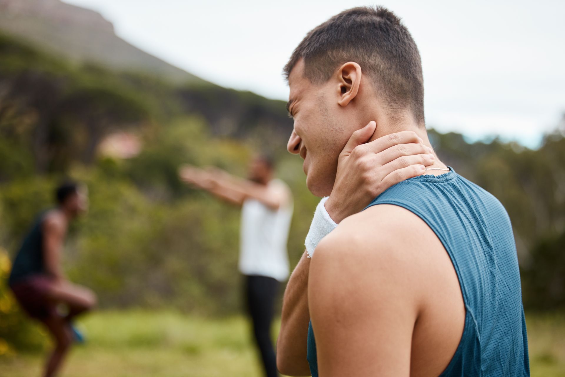 A man is holding his neck while a woman stands in the background.