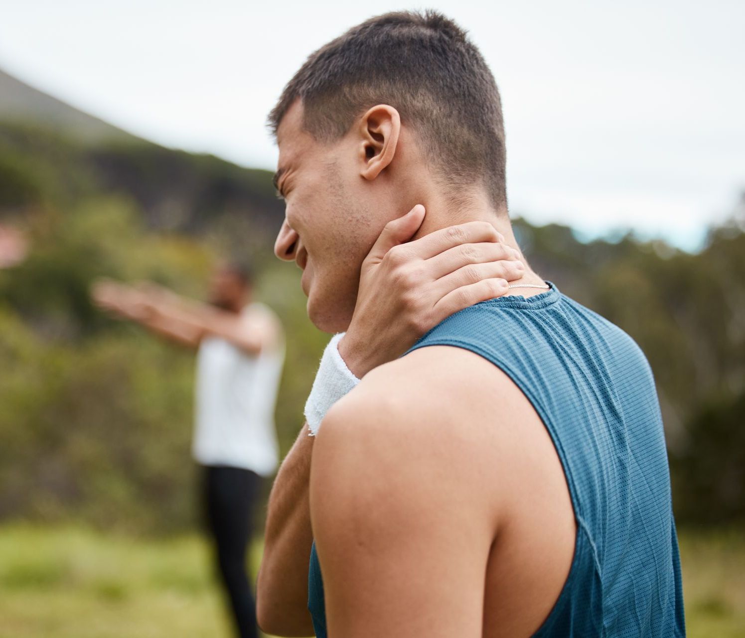 A man is holding his neck in pain while another man stretches in the background.