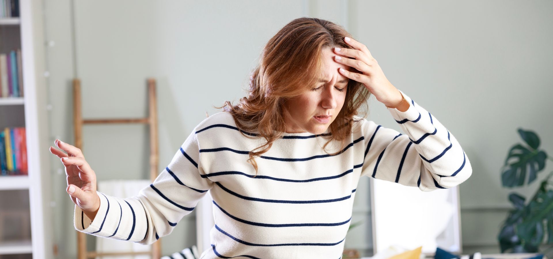A woman in a striped sweater is holding her head.