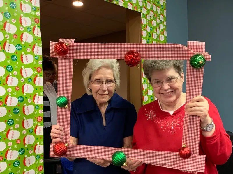 Two Happy Senior Women Posing with Handheld Christmas Ornament Frame