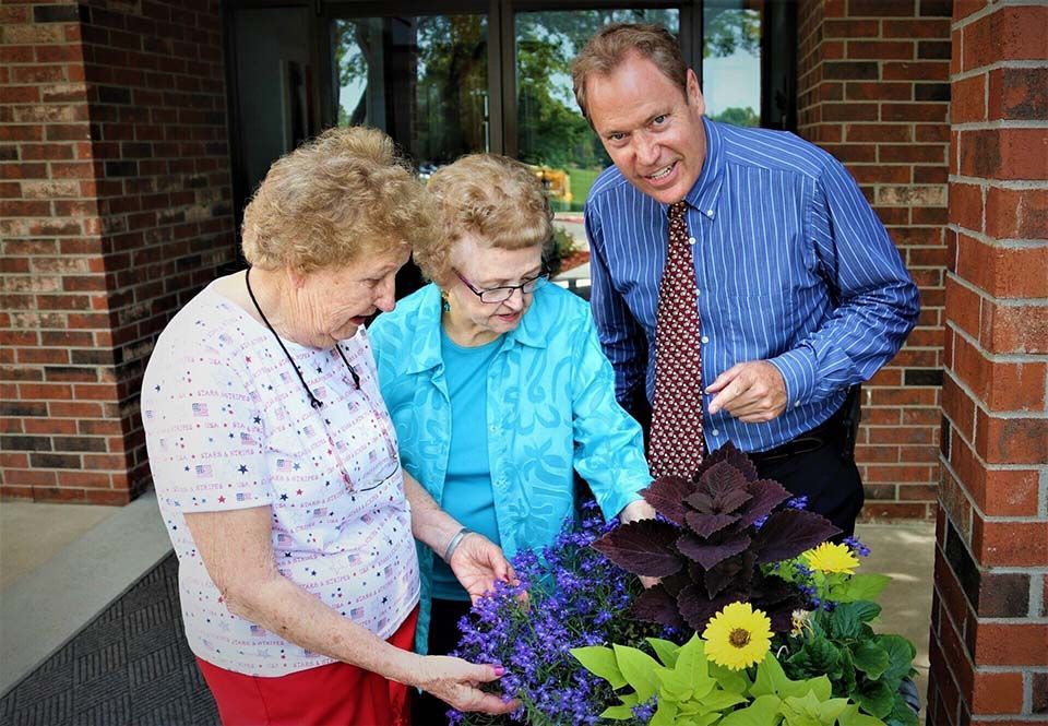 Two people standing with a man outside a brick building, all looking at a vibrant potted plant.