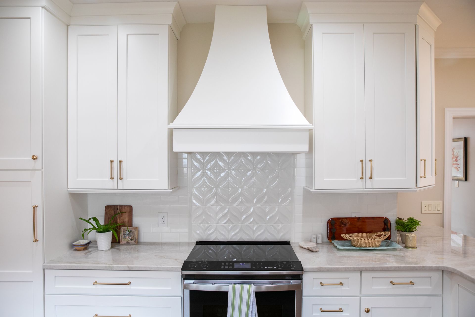 White kitchen with range hood, cabinets, and patterned backsplash.