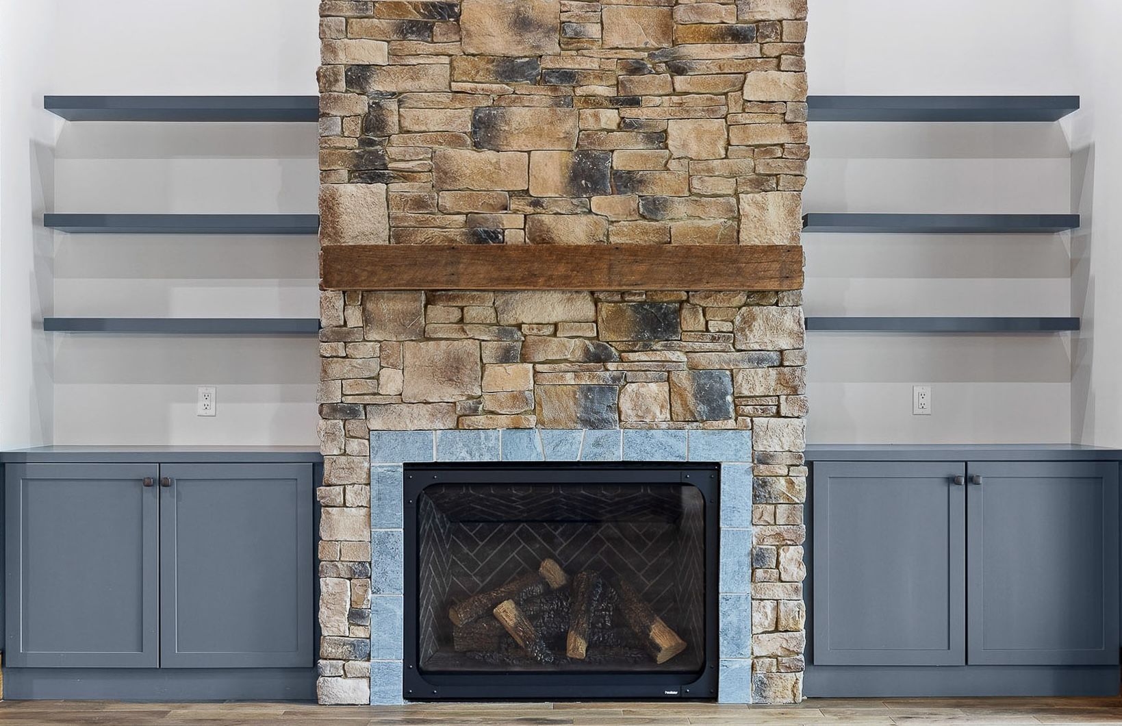 Fireplace with stone surround, built-in shelves, and blue cabinets.