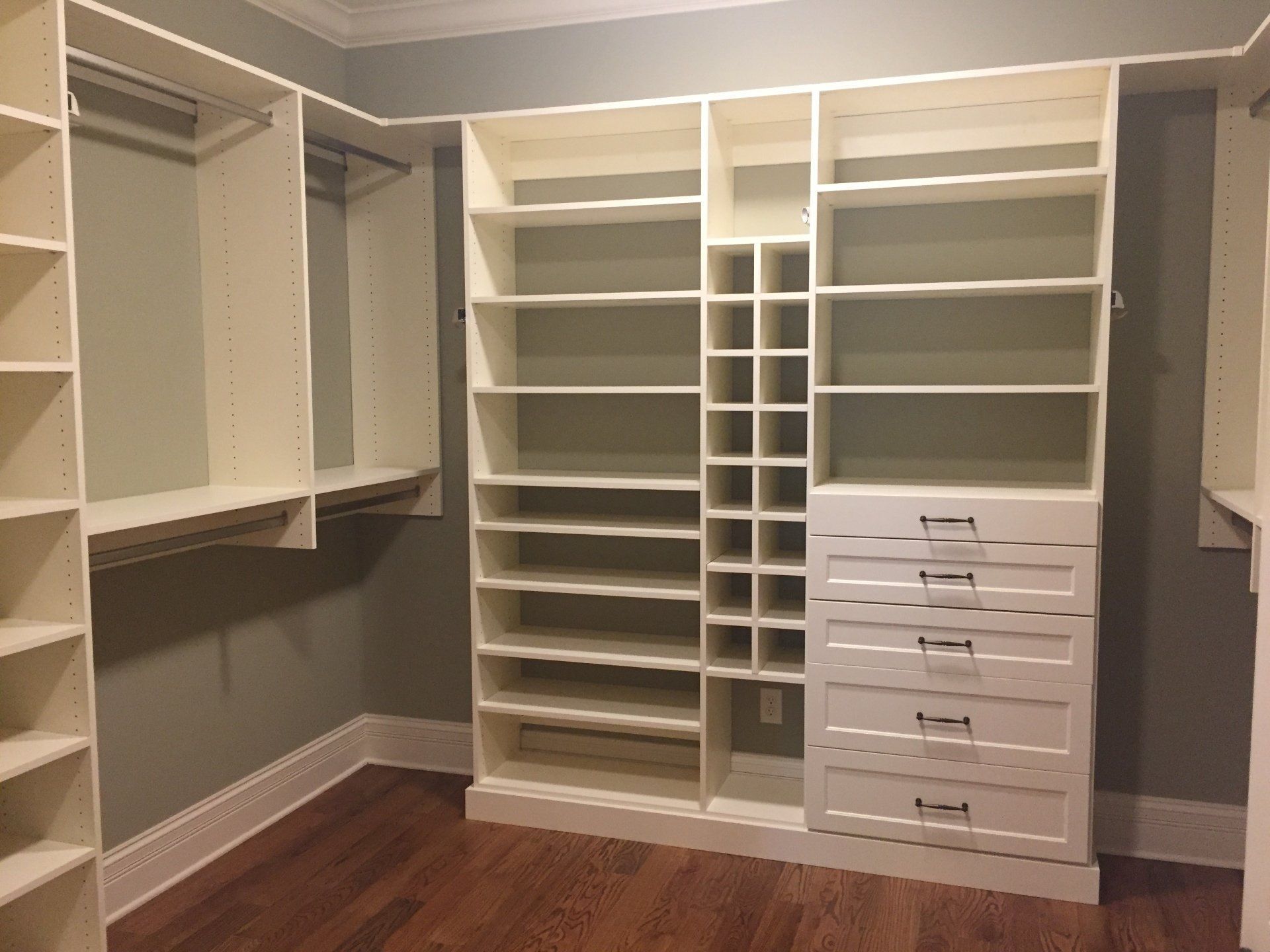 Walk-in closet with white shelving and drawers, wooden floor, and gray walls.