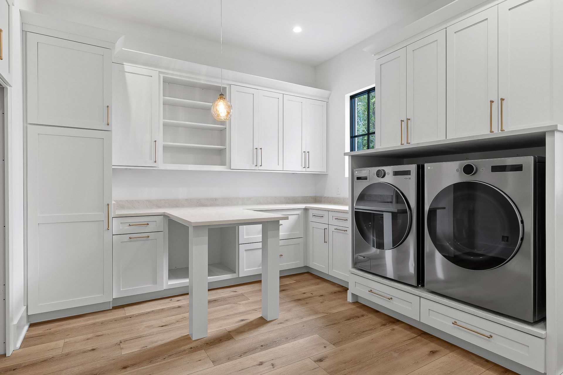 Bright, white laundry room with cabinets, a folding table, and stainless steel washer/dryer.