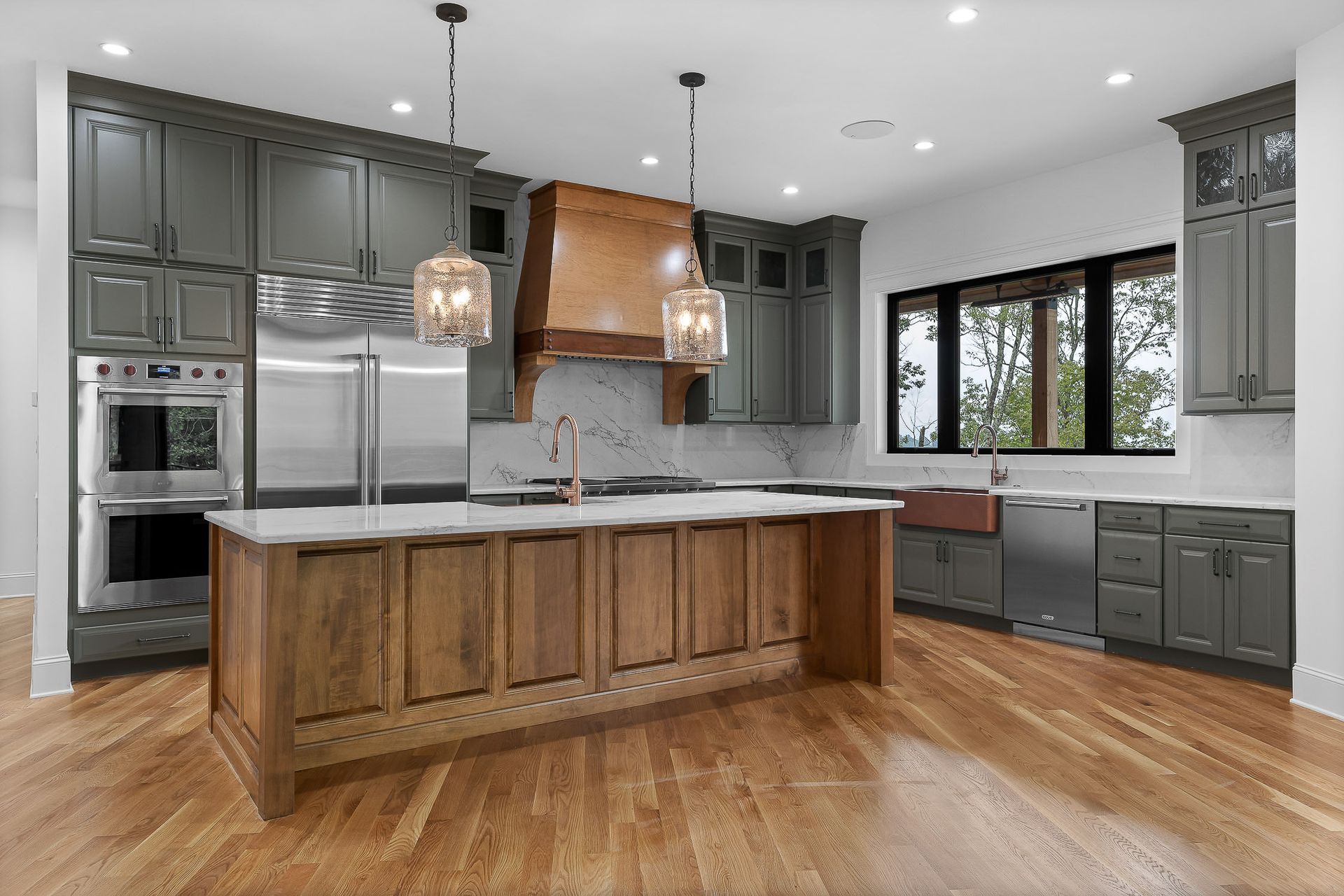 Modern kitchen with gray cabinets, wooden island and range hood, and stainless steel appliances.