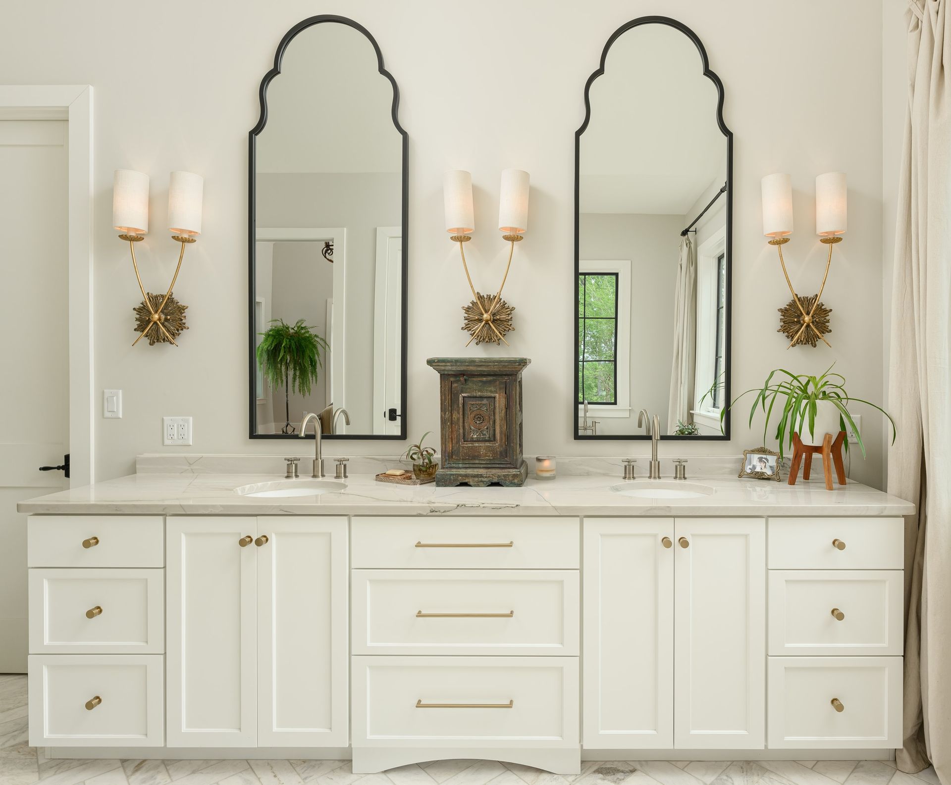 Elegant white bathroom with double sinks, arched mirrors, and gold accents.