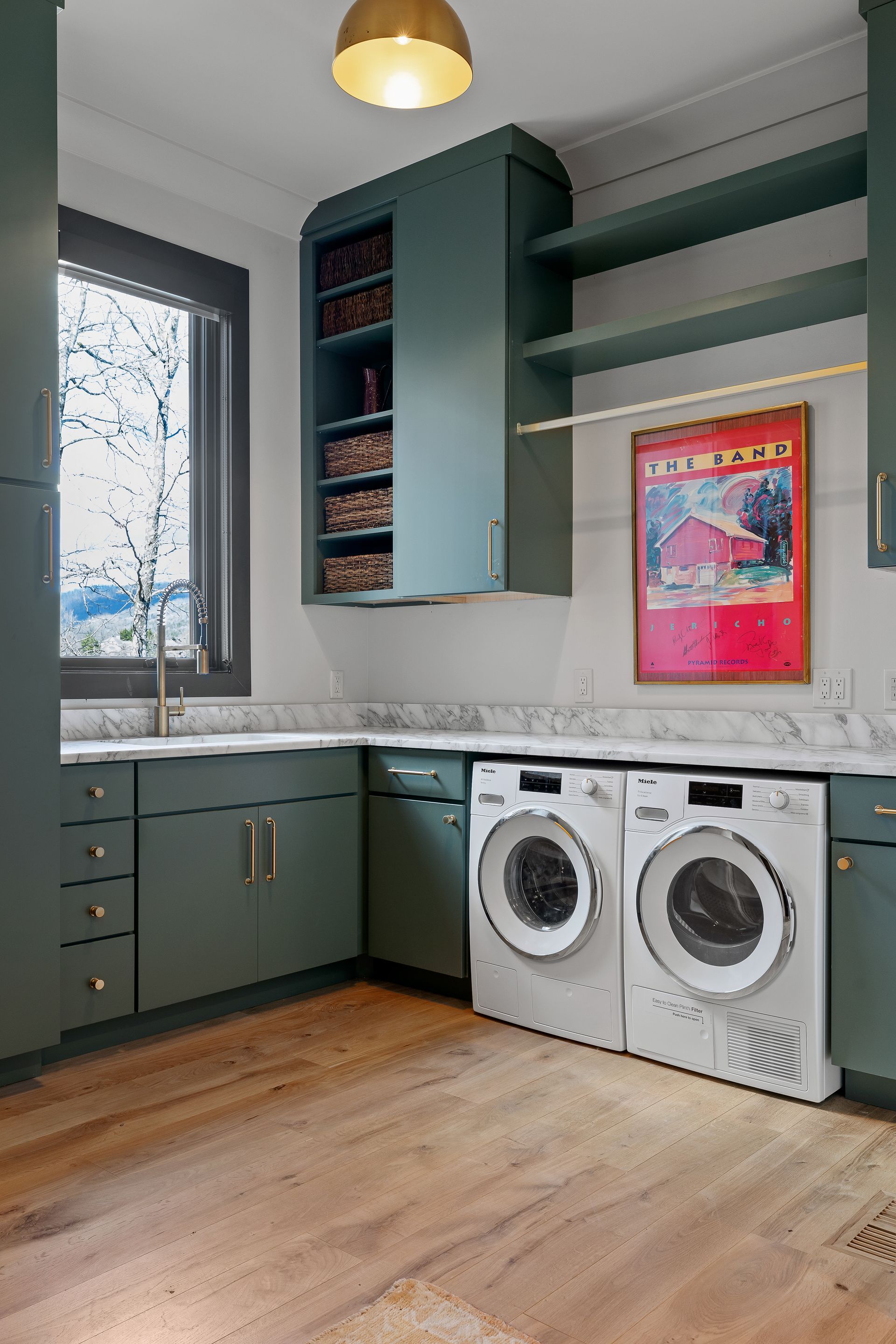 Green laundry room with white appliances, wood floors, and marble countertop, next to a window.